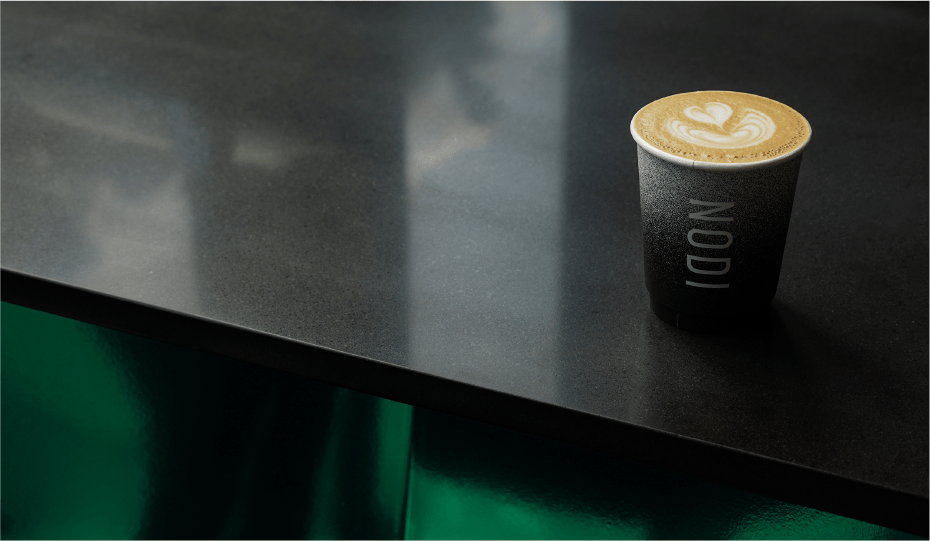 A NODI coffee cup on a dark counter