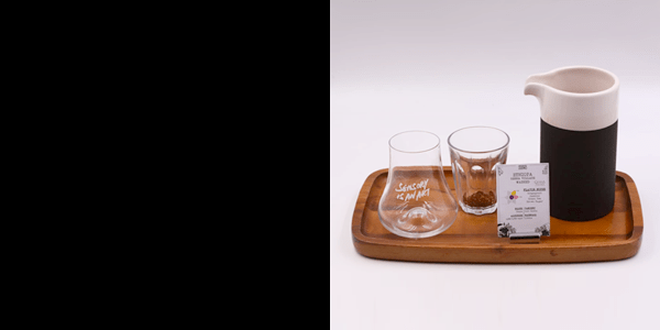 A wooden tray with tasting glasses, a coffee carafe and a sensory ZERO tasting card