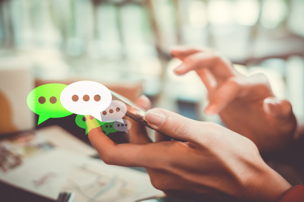 A hand tapping a phone with green and white chat bubbles floating above it